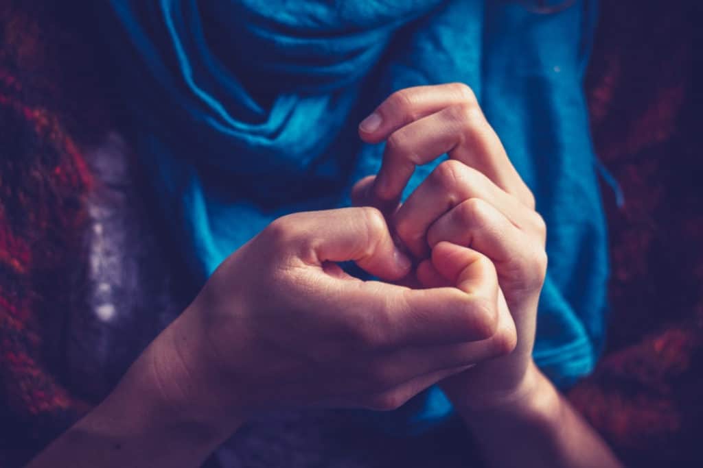 Close-up of woman's hands picking at her fingernail bed.