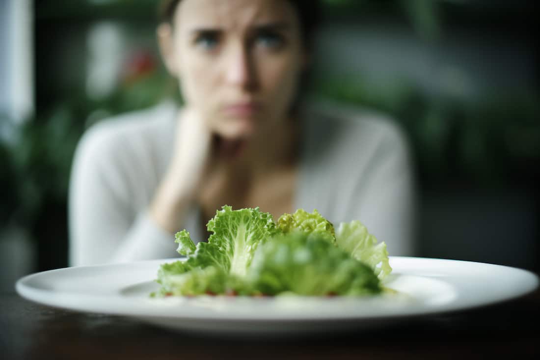 Salad on plate on table with blurry frustrated woman on diet in background
